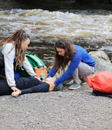Two people tending to a person lying on the ground by a river