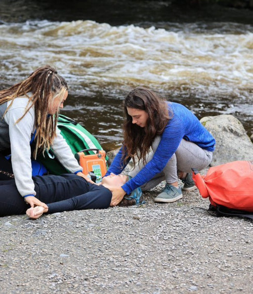Two people tending to a person lying on the ground by a river