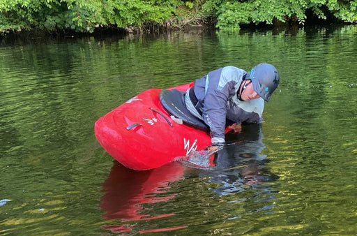 Person in a red kayak on a calm body of water with greenery in the background