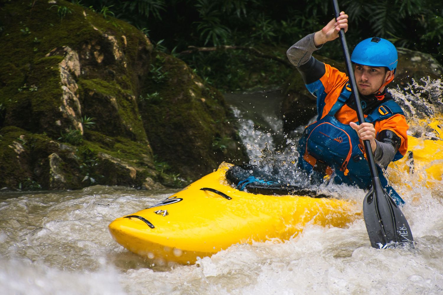 Person kayaking in rapids with a helmet and life jacket