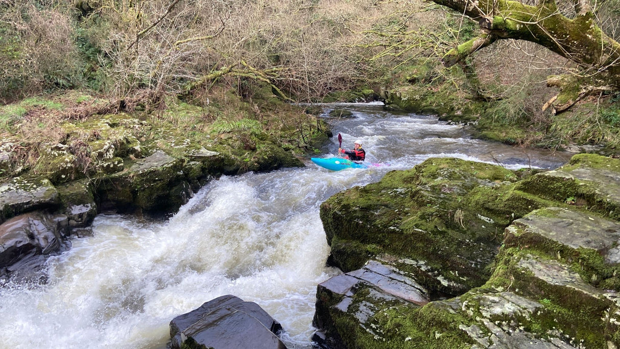 Person kayaking through a rocky river with greenery on either side