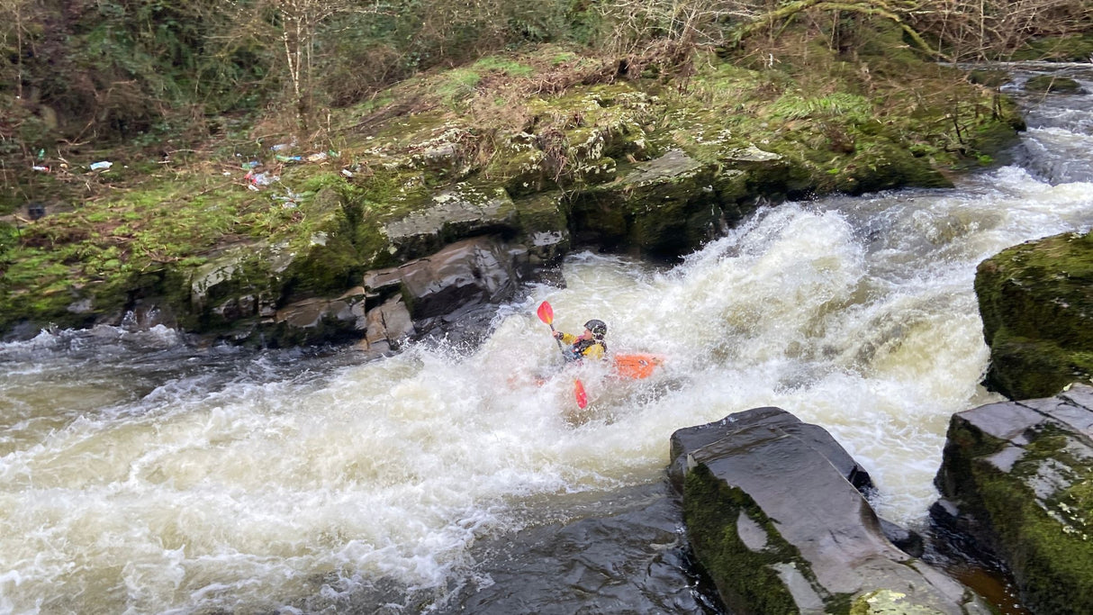 Person kayaking through rapids in a forested area